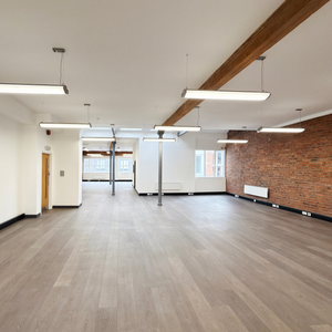 Whole floor for rent in Manchester. Large room with wooden flooring, white walls, and a brick wall section.