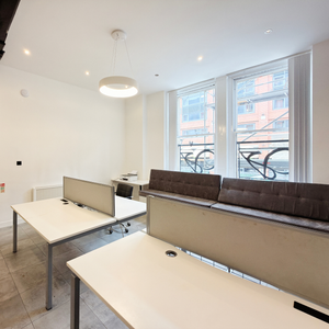 Modern office space for rent with desks and a bench by large windows. Located at Portland St. Manchester.